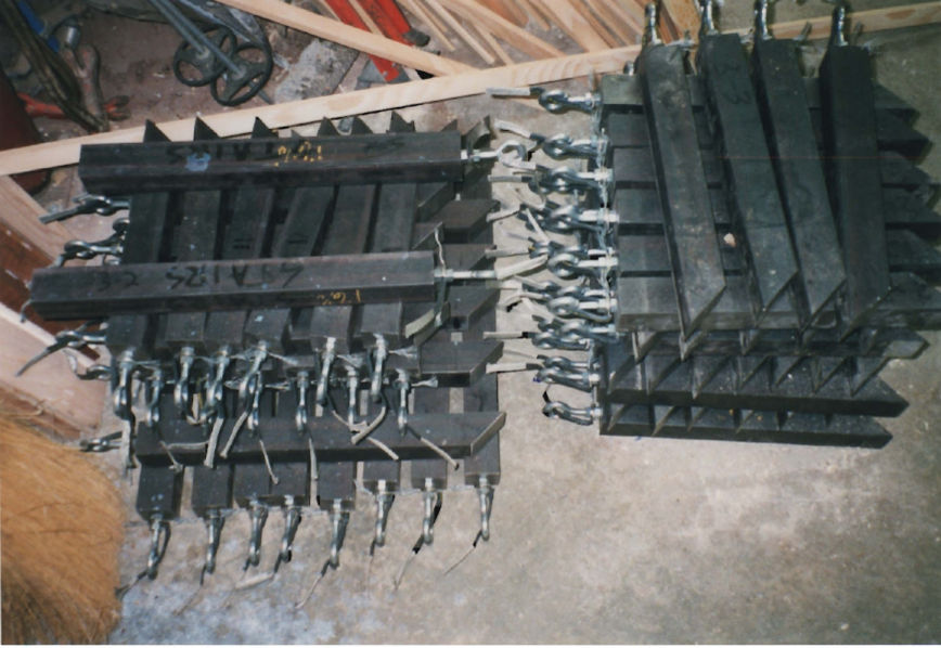 Custom-cut steel sash weights laid out in rows, each fitted with a chain clip